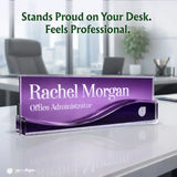 A personalized acrylic desk nameplate with a purple gradient design and the text 'Rachel Morgan Office Administrator', displayed on a white desk in a blurred office setting with the text 'Stands Proud on Your Desk. Feels Professional.