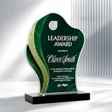 A custom acrylic award trophy plaque with a wavy silhouette, featuring a dark green front panel with white text, a gold glitter accent strip, and a black rectangular base, shown on a white background.